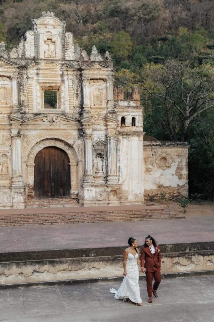 AlexJose-DestinationWedding-AntiguaGuatemala-2026-Zsanettkphoto-133 Wide shot of the ruins facade at Ermita de la Santa Cruz with the couple walking away - a romantic post-wedding ceremony moment.